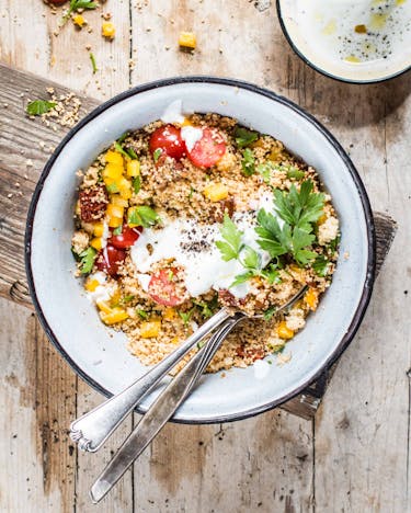 Couscous mit buntem Gemüse und Petersilie in weißer Schale mit Joghurt-Dip auf Holzuntergrund