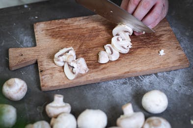 Chapignons werden auf Holzbrett für Pizza funghi geschnitten