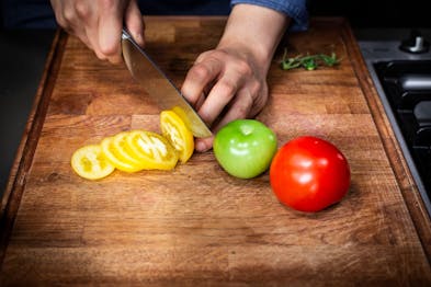 eine gelbe Tomate wird in Scheiben geschnitten. Daneben eine grüne und eine rote Tomate