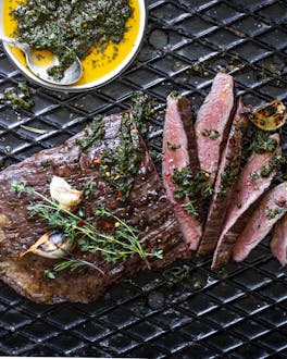 Steak medium rare gegrillt auf schwarzem Blech mit Chimichurri Dip in gelber Schale.