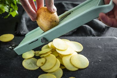 Eine Kartoffel wird in dünne Streifen gerieben.