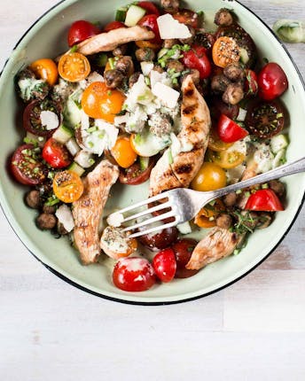 Tomaten-Kichererbsen-Salat mit würzigen Hähnchenstreifen auf hellem Untergrund