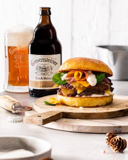 Burger auf Holzbrett neben Bierflasche und Bierglas