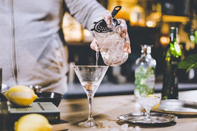 Der Dry Martini wird durch einen Strainer aus dem Rührglas in das Martiniglas gegeben.