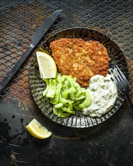 Backfisch mit Remoulade und Gurkensalat auf schwarzem Teller auf Grillrost