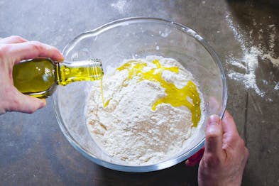 Glasschüssel mit Mehl in die Olivenöl aus Glasflasche gegeben wird
