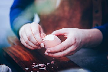ein Ei wird von zwei Händen über einem Holzbrett gepellt