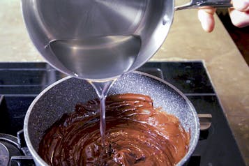 Geschmolzene Kakaobutter aus einem Topf zur geschmolzenen Nuss-Nougat-Creme geben