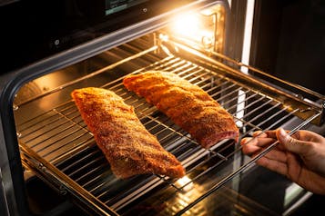 Schhweinerippchen auf einem Küchengitter werden in den Ofen geschoben