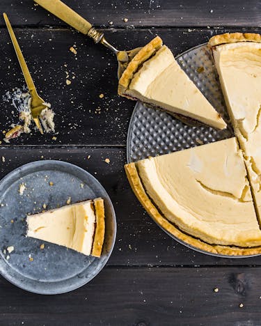 Aus einem gelben Käsekuchen sind mit Goldbesteck drei Stücke geschnitten und auf dunkelgraue Teller gelegt worden