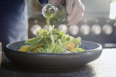 Kräuterdressing wird über den Salat in einer schwarzer Schüssel gegeben.
