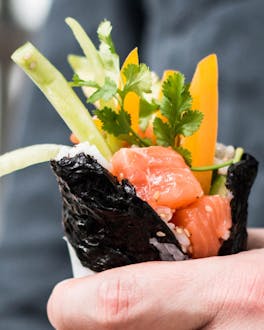 Sushi als Burrito aufgerollt mit Lachs und Gemüse in einer Hand gehalten