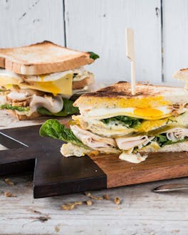 Zerteiltes Hühnchen-Sandwich mit Käse und Ei auf Holzbrettchen mit Holzspießen aufgespießt.