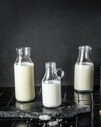 Sechs verschiedene pflanzliche Milch-Alternative in kleinen Glasflaschen stehen vor einem schwarzen Hintergrund
