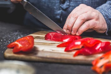Rote Paprika wird auf einem Holzbrett in Scheiben geschnitten