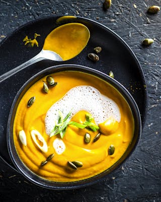 Süßkartoffel-Curry-Suppe mit Kokosmilchschaum und Kürbiskernen von oben fotografiert auf dunklem Untergrund.