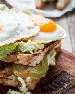 Club Sandwich mit Hähnchen, Salat und Spiegeleiern auf einem Holzbrettchen