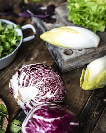 Verschiedene Salatarten, darunter Chicorée, Radicchio, Endivie und Feldsalat liegen zur Weiterverarbeitung auf einem Holztisch
