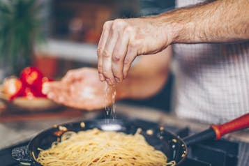 Hand streut Salz über Spaghetti in einer Pfanne