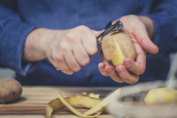 Es sind zwei Hände zu sehen, die eine Kartoffel schälen.