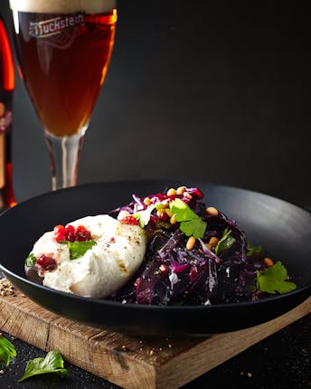 Ein schwarzer Teller mit Burrata auf Rotkohl mit Preiselbeersauce neben einer Flasche und einem Glas mit Duckstein