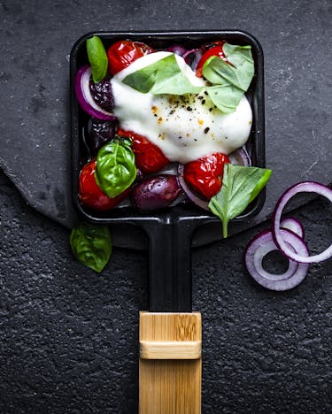 Italienisch befülltes Raclette-Pfännchen mit Tomate, Zwiebel, Mozzarella und Basilikum