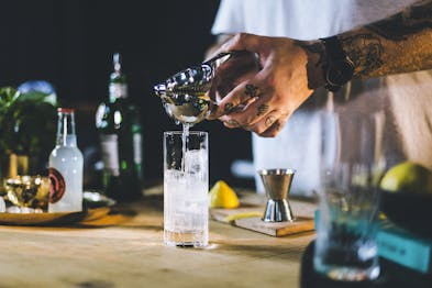 Barkeeper presst Zitronensaft in Highball Glas mit Eiswürfeln