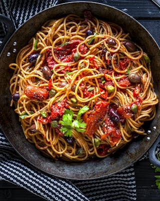 Spaghetti Puttanesca in Pfanne auf schwarzem Tisch