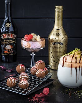 Drei Flaschen Baileys und dazugehörige Dessert-Kreationen wie japanische Pancakes mit Karamellsauce, Pralinen, rosa Tiramisu im Glas und Dalgona Coffee.