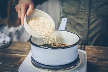 Quinoa wird in einen Topf auf einer Kochplatte gegeben