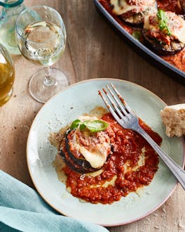 Auberginen-Parmigiana-Türmchen mit Tomatensauce auf Teller, daneben liegt Brot