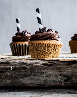 Cupcakes mit flüssigem Kaffeekern und einer schokoladigbraunen Cremehaube mit Kaffeebohnen auf einem dicken Holzbrett