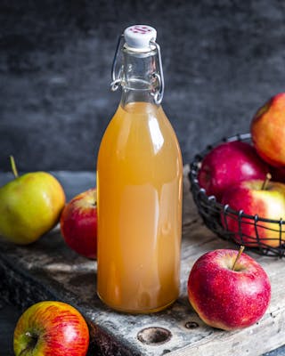 Apfelessig in Glasflasche auf Holzbrett mit ganzen Äpfeln