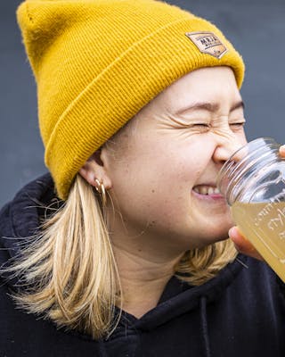 Frau mit gelber Mütze verzieht beim Apfelessig trinken das Gesicht