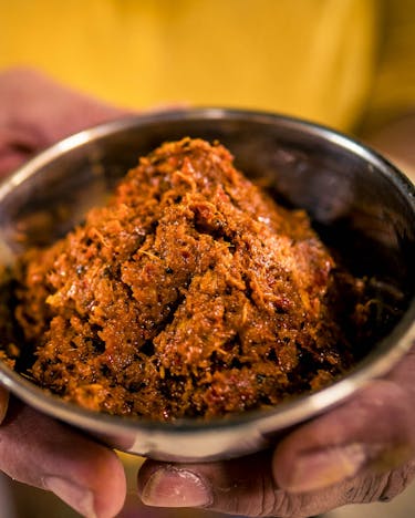 Eine Metallschüssel mit roter Currypaste wird von zwei Händen gehalten
