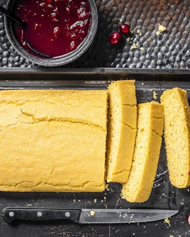 Gelbes Maisbrot auf schwarzem Tablett, dazu Cranberry-Sauce.