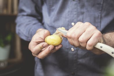 Kartoffel wird mit einem weißen Messer in der Hand gepellt