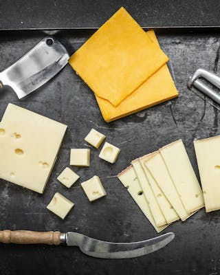 Cheddar, Edamer und anderer Käse auf schwarzem Untergrund mit Käsemessern