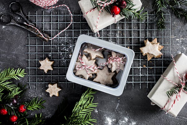 Plätzchen in einer Keksdose mit weihnachtlichem Schmuck sowie einer Schere und rot-weißer Schnur