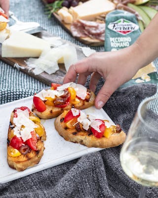 Hände greifen Bruschetta mit Tomaten, Datteln und Pecorino auf Picknickdecke