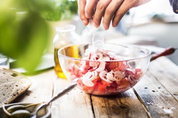 In einer Glasschüssel wird ein Tomatensalat zusammengemischt.