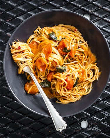 Spaghetti mit Tomatensauce, frischen Tomaten und Basilikum in schwarzer Schale.