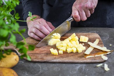 Kartoffel wird auf Holzbrett mit Messer gewürfelt