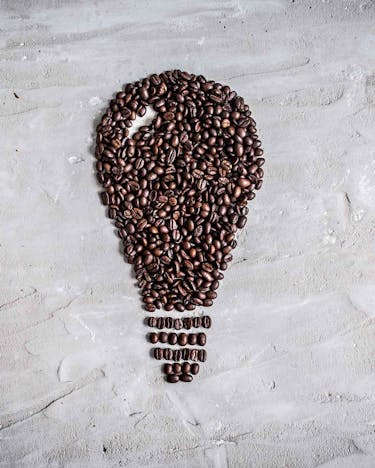 Eine Glühbirne von oben, die aus einzelnen Kaffeebohnen zusammengelegt wurde