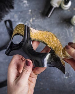 Goldglitzer auf schwarzer Karnevalsmaske verteilen