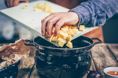 Kartoffelwürfel werden von einem Brett in einen Kochtopf gegeben.