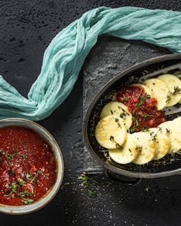 In einer Auflaufform liegen Gnocchi, daneben eine Schale mit Tomatensauce