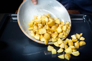 Kartoffelwürfel werden aus einem hellen tiefen Teller auf ein Backblech geschüttet