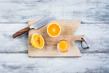 Orangenhälften und gepresster Orangensaft sowie ein Messer auf einem Holzbrett