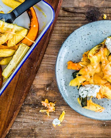 Schupfnudeln mit Kürbis und Zucchini überbacken mit Käse auf einem grau-blauen Teller auf Holzuntergrund.
